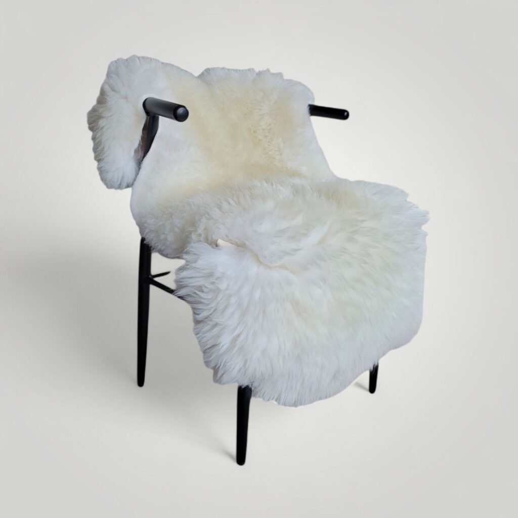Large white fluffy sheepskin used as a cozy seat cushion draped over a wishbone chair